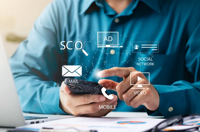 Business professional using mobile phone with digital icons for SEO, ads, social media, video, email, and mobile marketing, representing digital advertising strategies to drive ROI.
